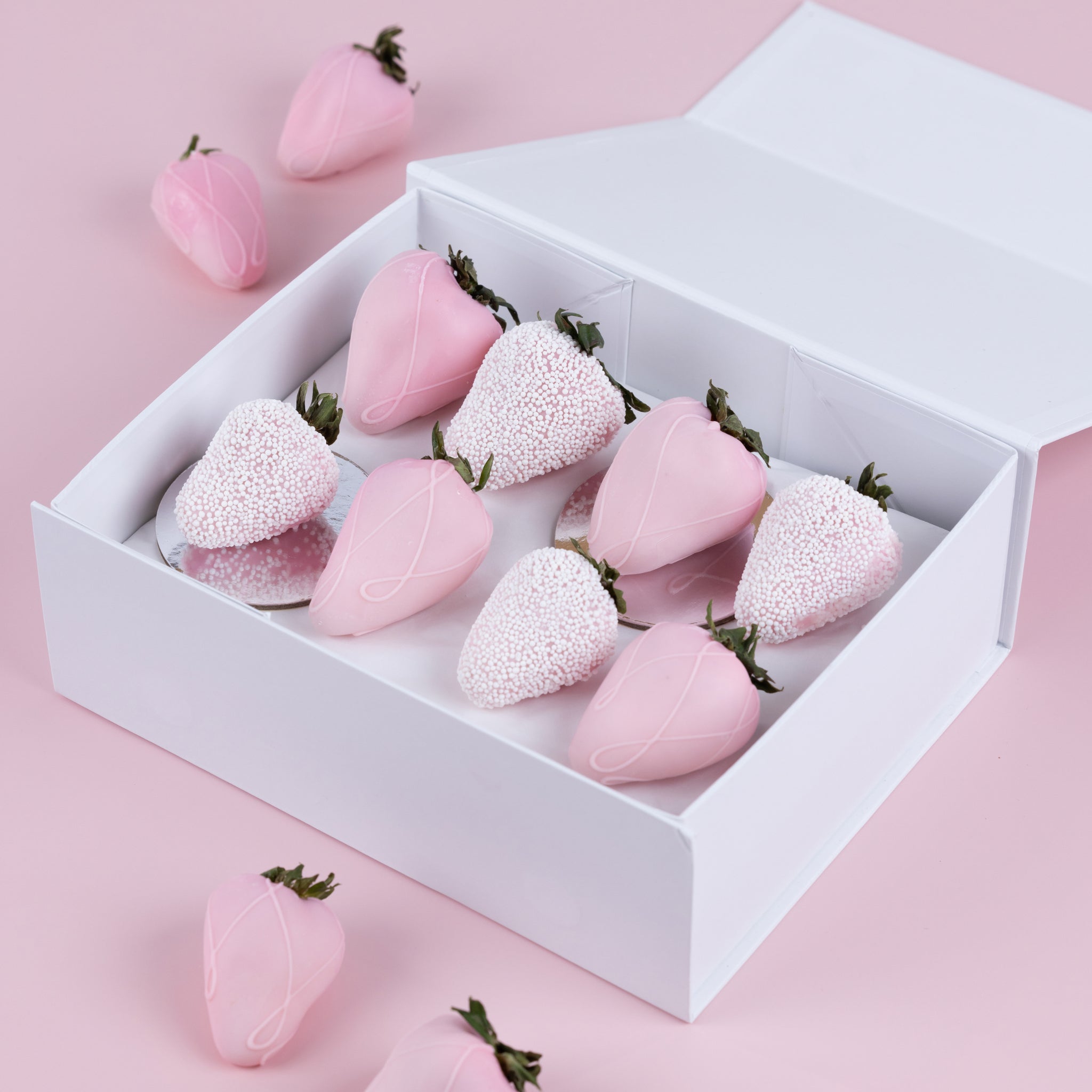 A white gift box with an assortment of pink, chocolate dipped strawberries with swirl patterns and edible pearls