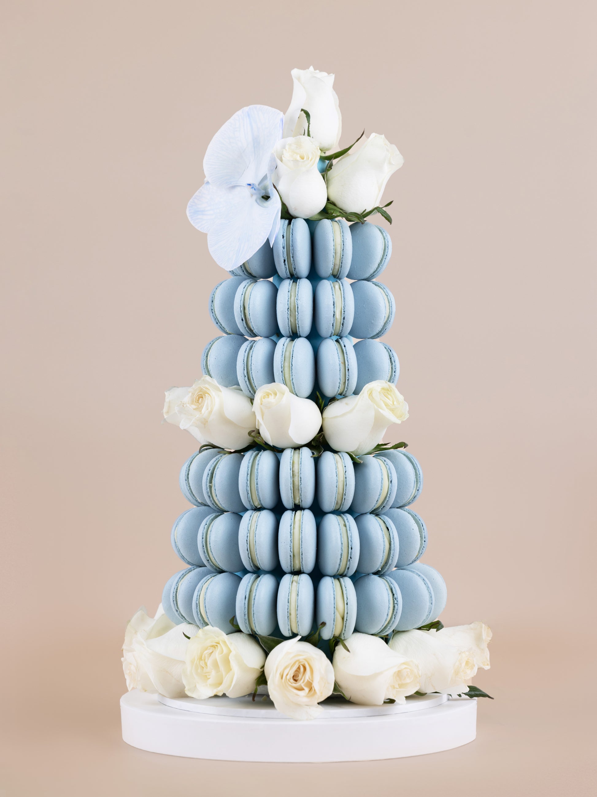 A tower made of baby blue coloured, handmade macarons with orchids and fresh, white Colombian roses placed within the tower