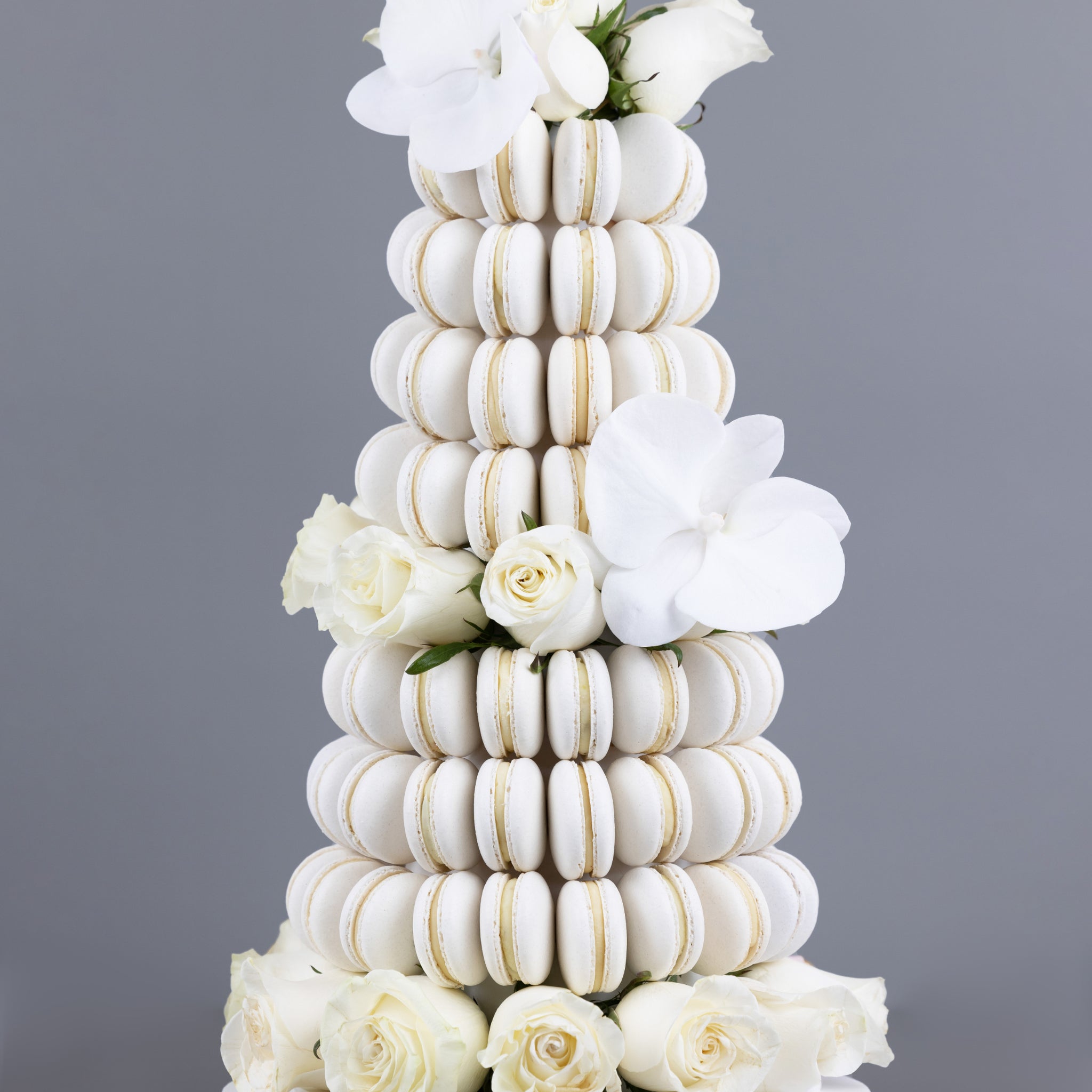A tower made of white coloured, handmade macarons with orchids and fresh, white Colombian roses placed within the tower