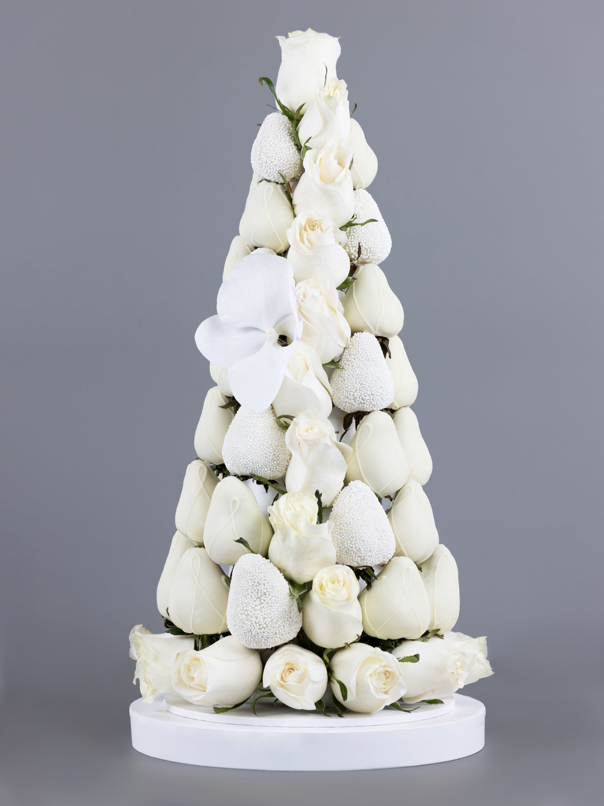 Tower made of white, chocolate dipped strawberries with white Colombian roses placed within and at the base of the tower and an orchid