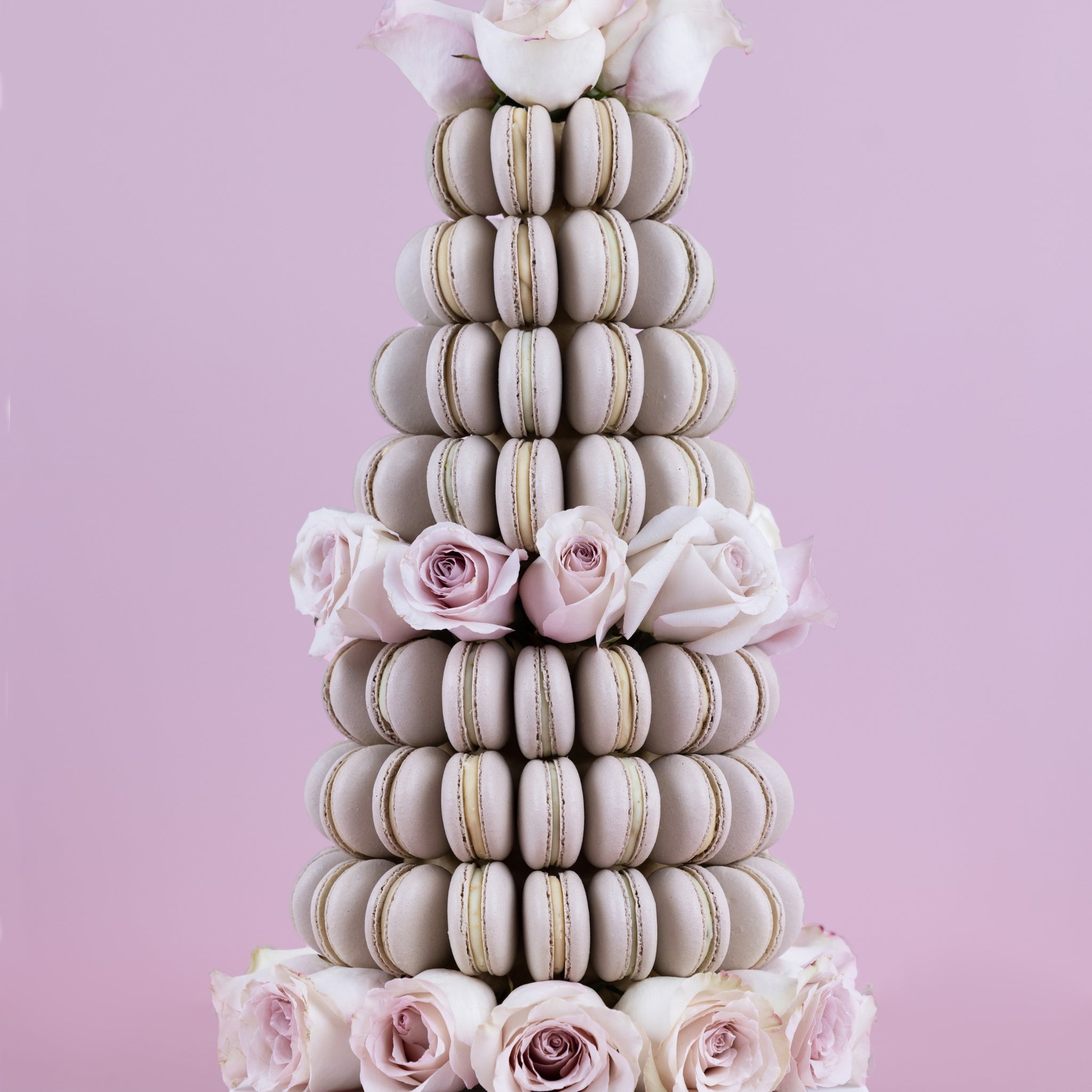 A tower made of champagne coloured, handmade macarons with fresh, white Colombian roses placed within and atop of the tower