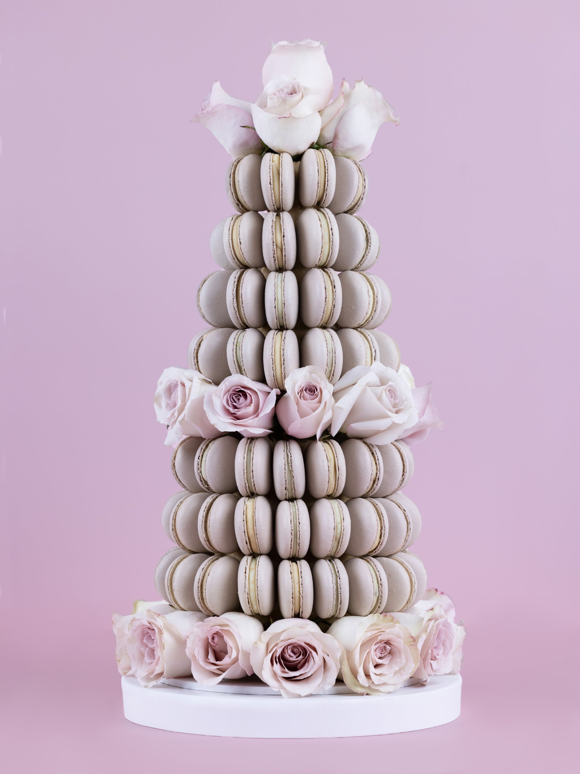 A tower made of champagne coloured, handmade macarons with fresh, white Colombian roses placed within and atop of the tower